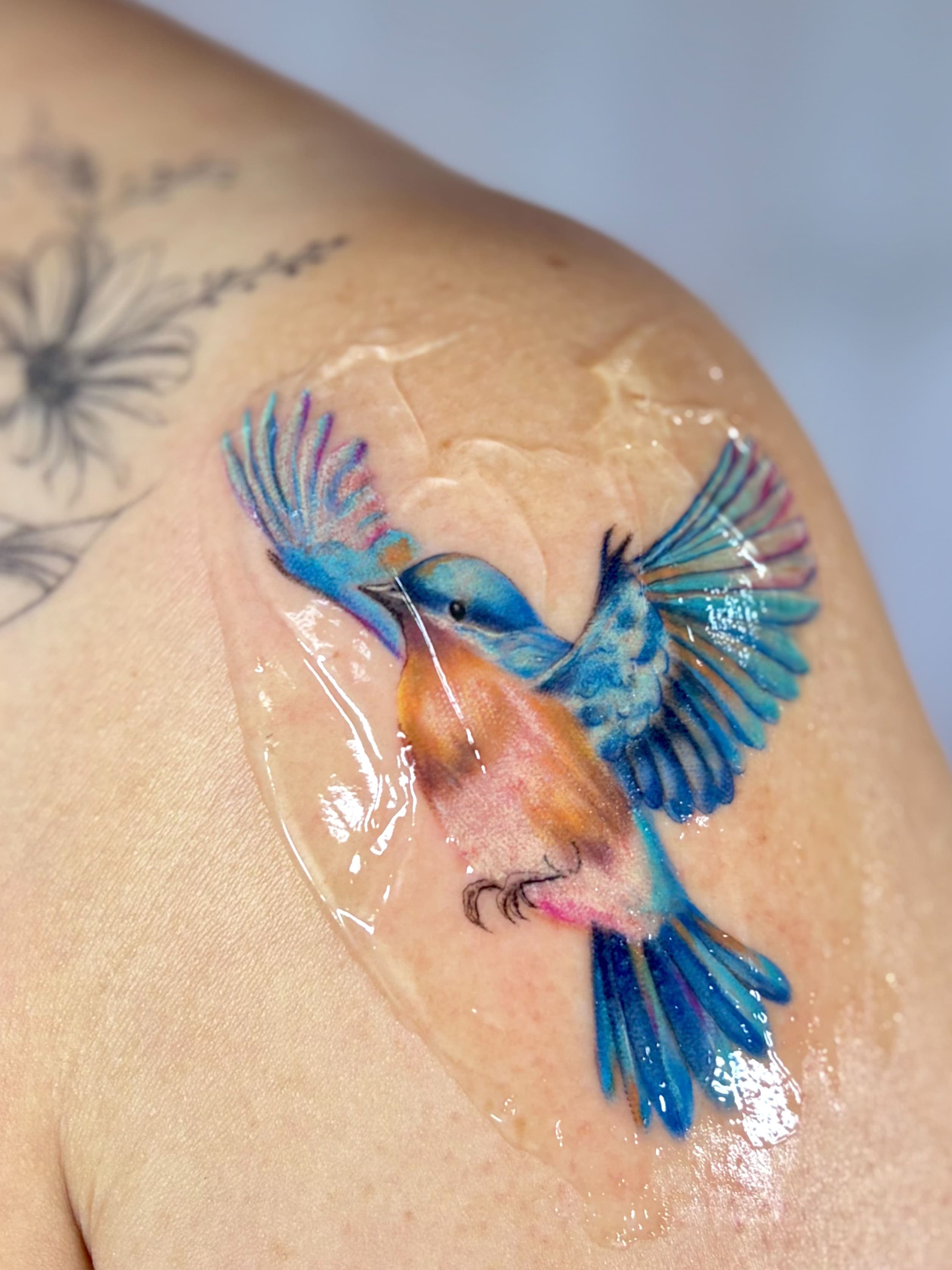 Tatuagem colorida de pássaro azul e laranja em voo